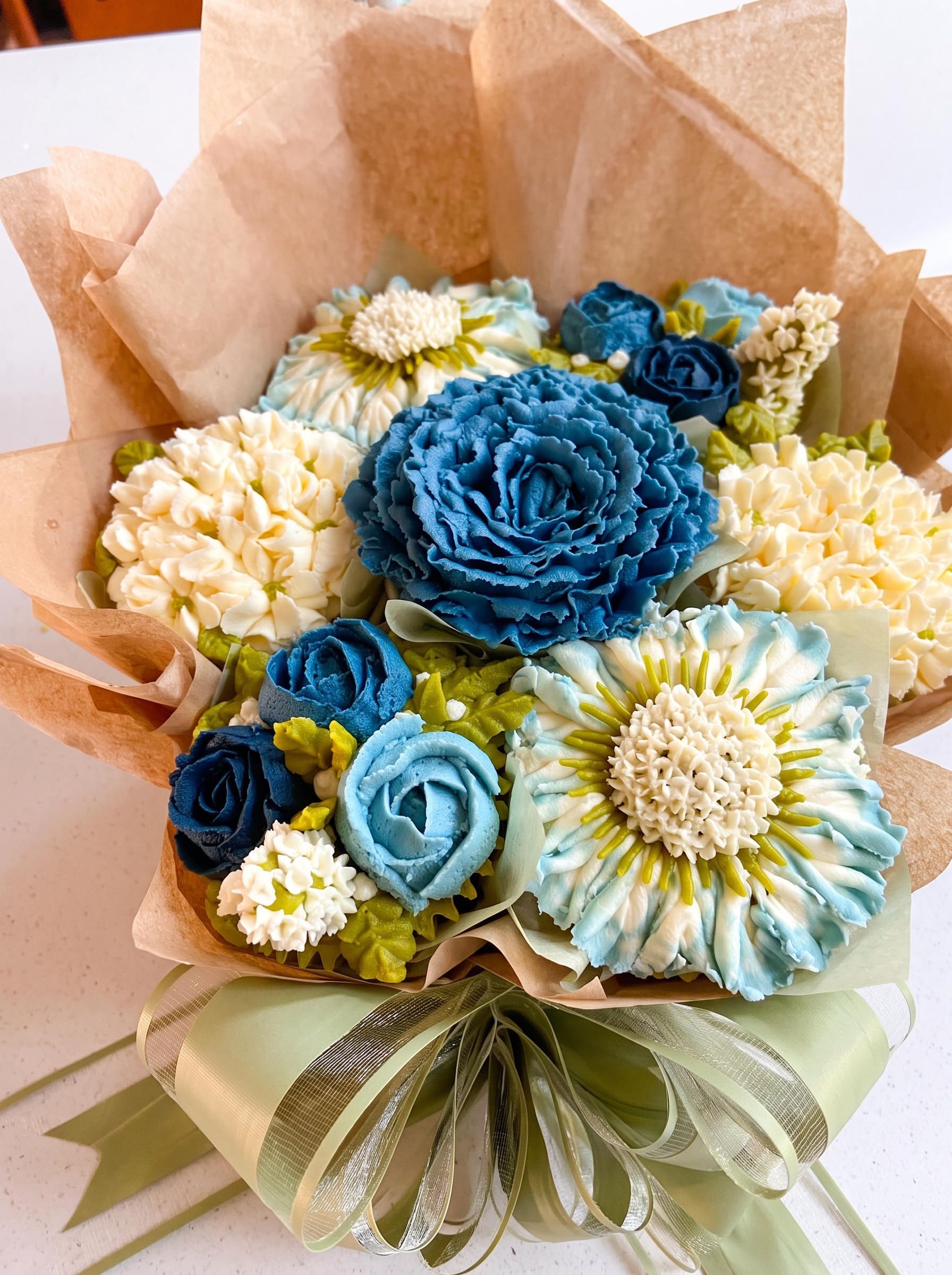 Summer Blooms cupcake bouquet with blue and cream buttercream flowers wrapped in kraft paper and sage ribbon