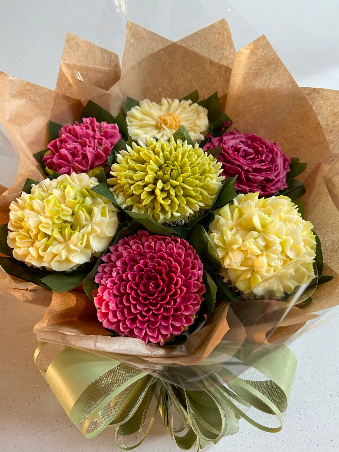 Bright cupcake bouquet with yellow and magenta buttercream flowers wrapped in kraft paper and sage ribbon