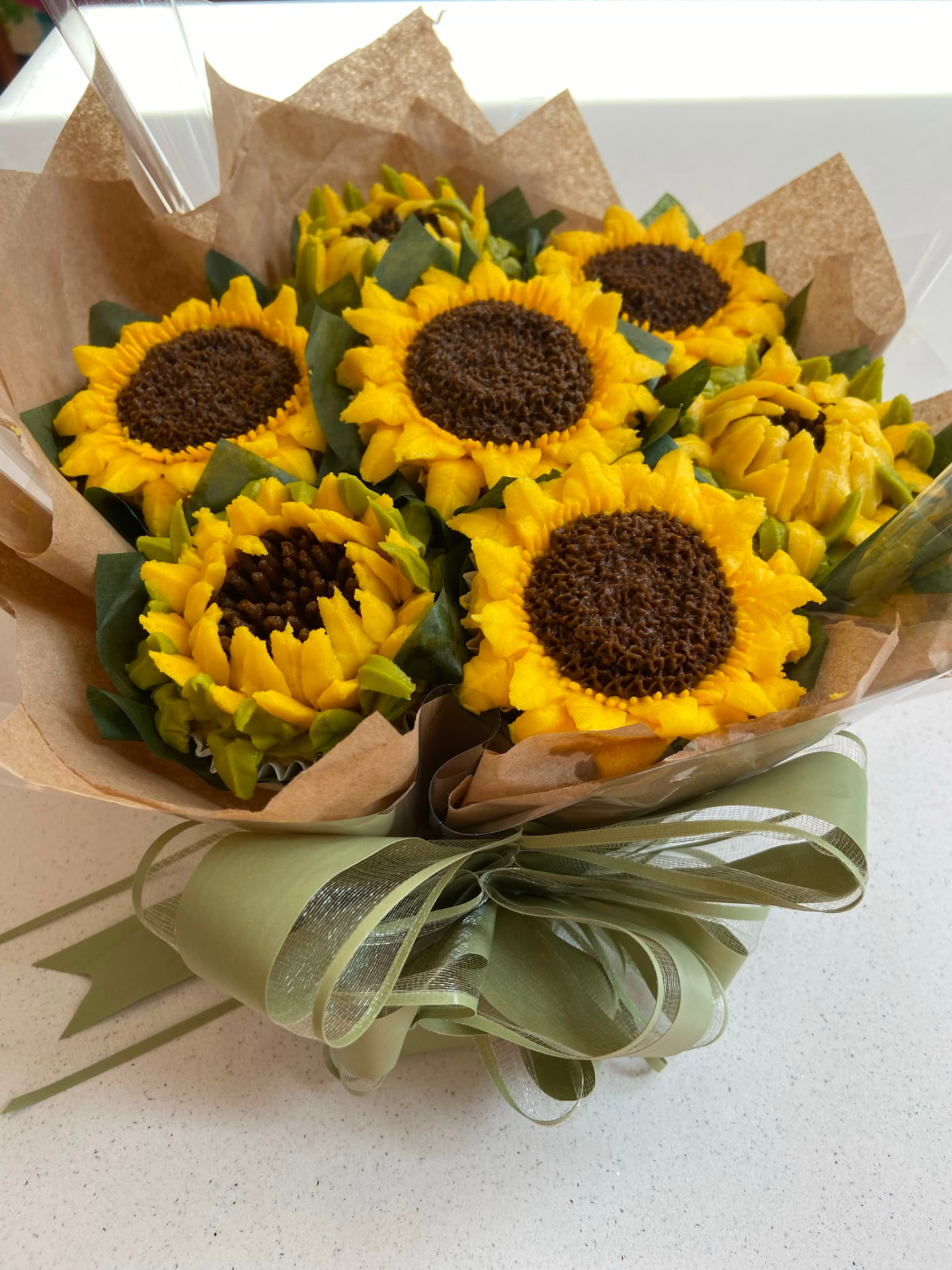 Sunflower cupcake bouquet with bright yellow petals and chocolate centres wrapped in kraft paper and sage ribbon